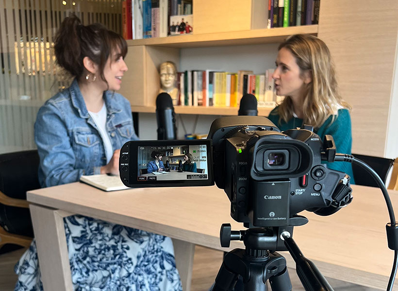 Two women talking at a table in front of a camera.