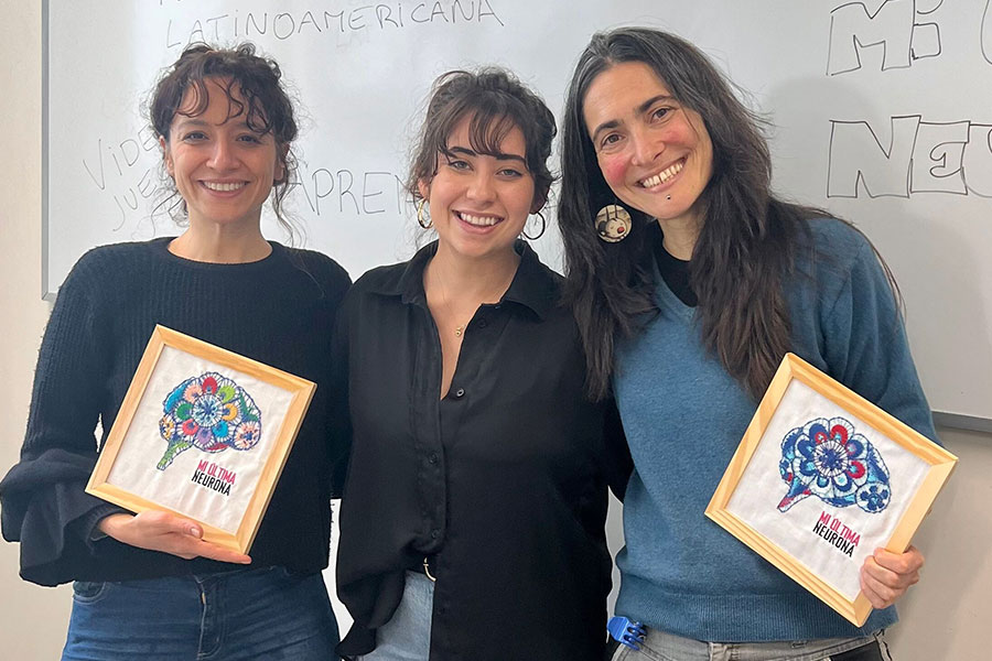 Three women smiling, two holding framed artwork.