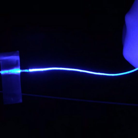 A blue glowing fiber in darkness. The fiber is held by finger and seems to light up with it touches another hand.