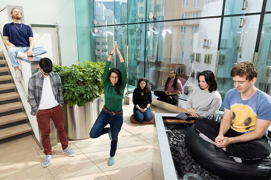 Seven people practicing different forms of mindfulness in a large room with floor to ceiling windows.