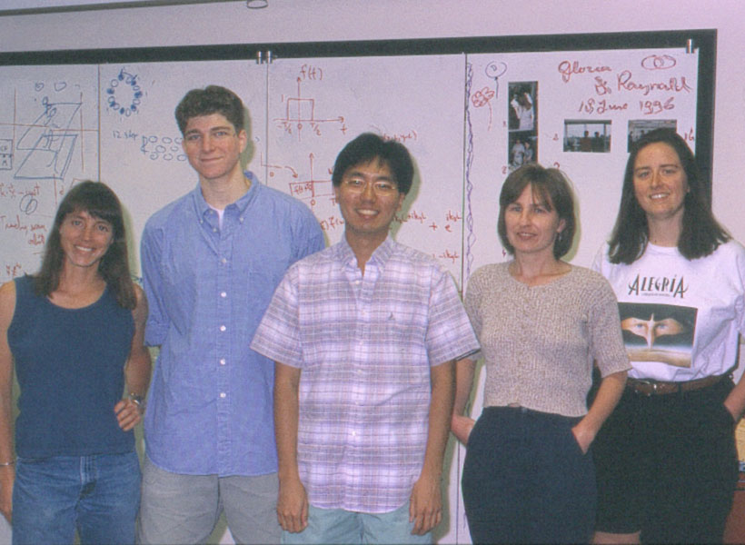 A group of five scientists standing and smiling in front of a whiteboard.