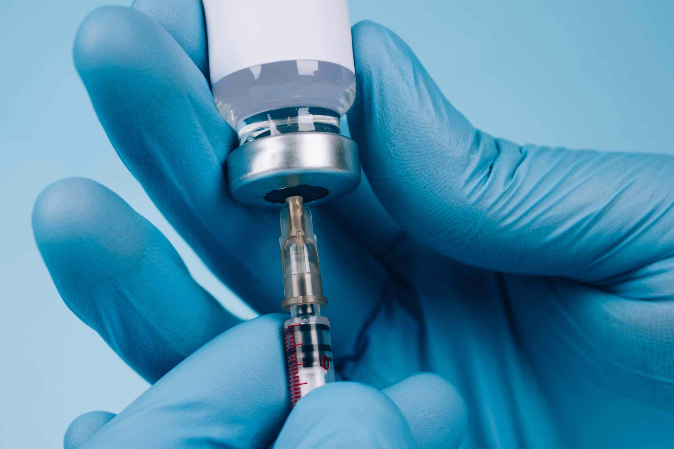Global vaccination concept. Doctor or scientist holding vial dose of common vaccine with syringe against blue background with copy space - prevention coronavirus. Selective focus, mockup image