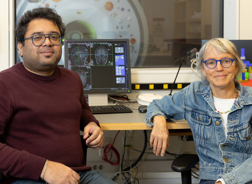 Male and female researchers sitting in an imaging center with an MRI in the background.