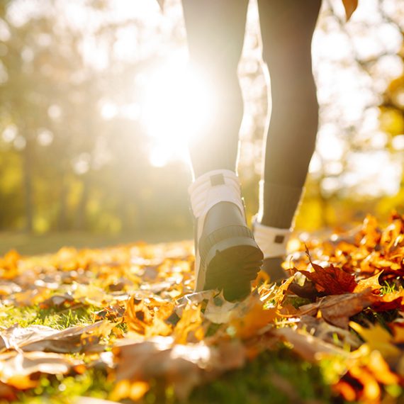 Close-up of female legs in hiking boots walks on ground with yellow-orange dry fall leaves during autumn season in park or forest. Feet walking in outdoor nature. Healthy lifestyle on leisure activity