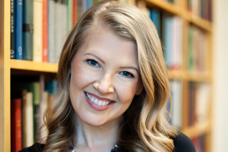 Woman smiling at camera in front of bookcase.