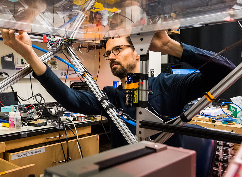 Man in blue shirt wearing glasses building a platform in a lab setting.
