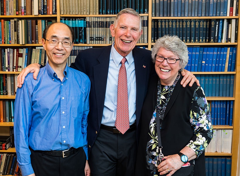 A group of three individuals standing in front of a bookcase.