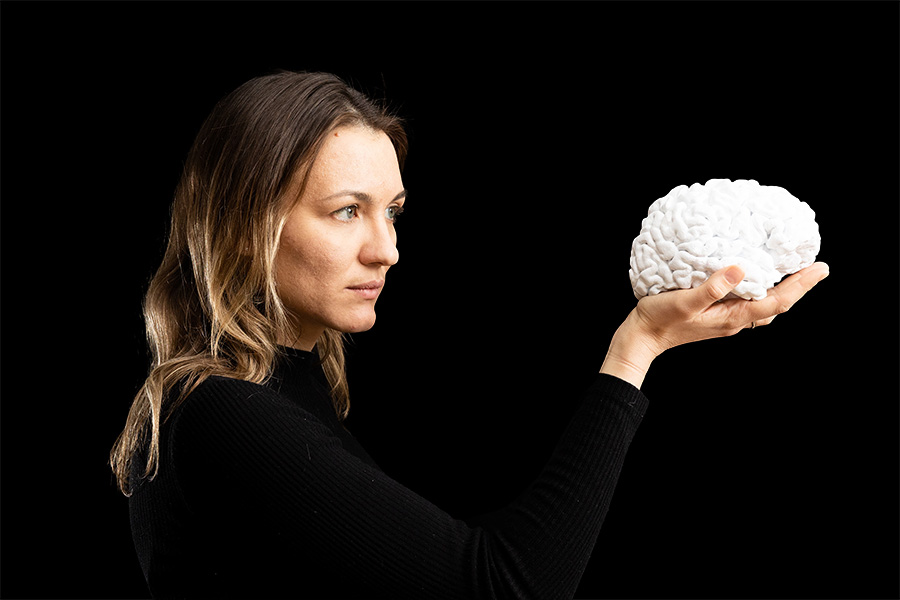 Woman holds a 3d printed white brain and looks intently at it.