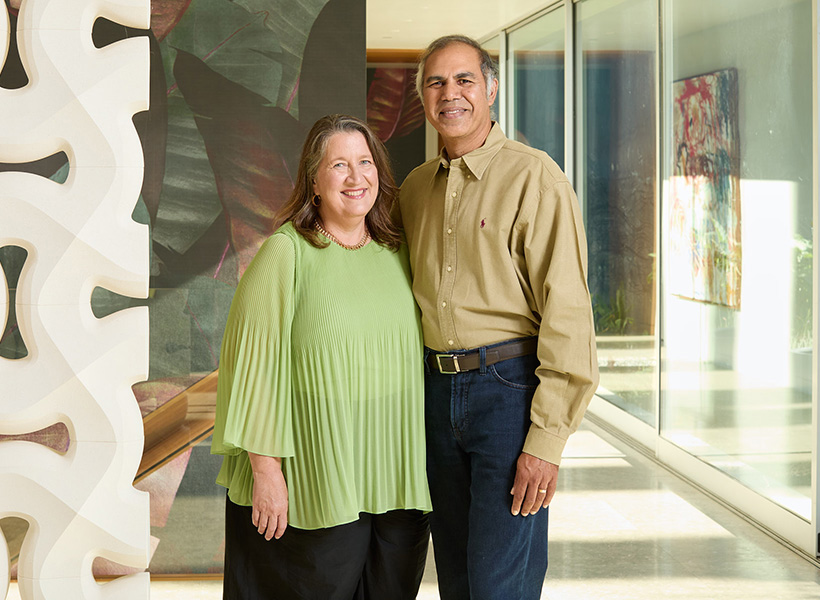 A smiling man and woman stand next to each other in a room filled with natural light.