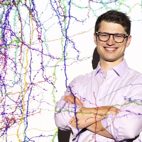 Sven Dorkenwald stands before a projection of the mouse connectome.
