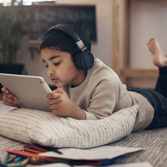 Shot of an adorable little boy using a digital tablet and headphones while completing a school assignment at home.