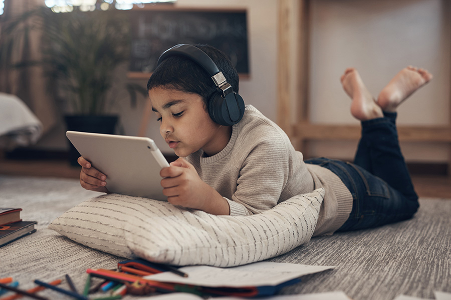 Shot of an adorable little boy using a digital tablet and headphones while completing a school assignment at home.