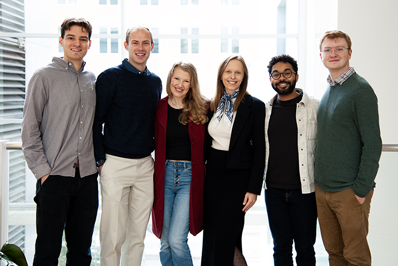 A group of smiling researchers stand in front of a wall of windows.