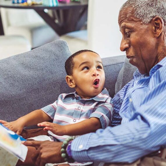 Toddler and grandfather reading a book and talking to each together.