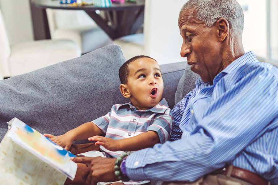 Toddler and grandfather reading a book and talking to each together.