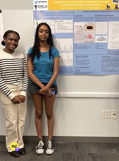 Two girls stand next to scientific poster.